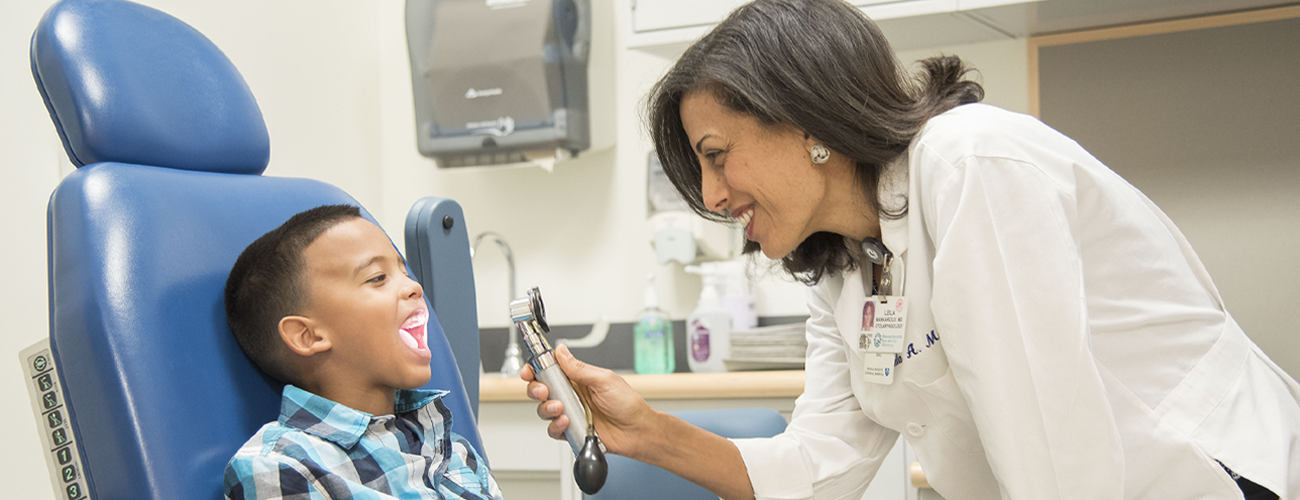 female doctor examining young boy's mouth in exam room